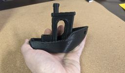 A large "Benchy", or 3D-printed tugboat model, in someone's hand. The print's layer lines are substantially thicker than typical.